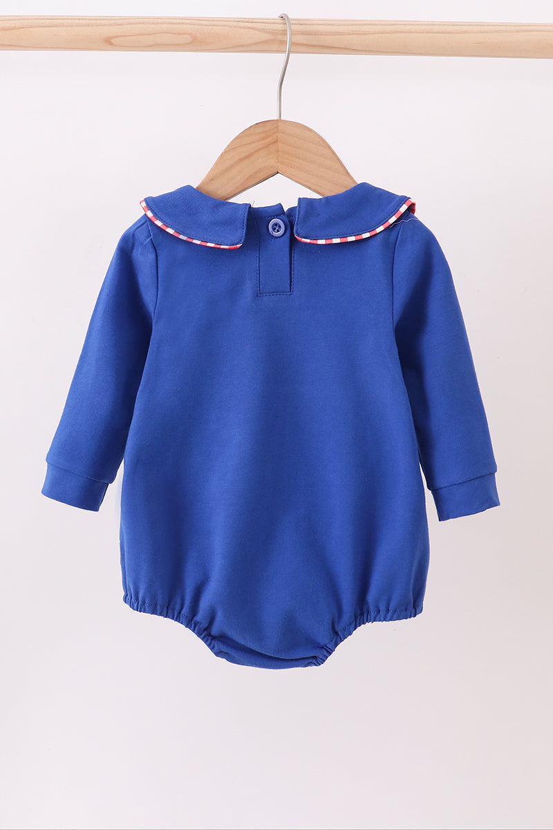 Blue baby romper with a red and white trim on a wooden hanger against a white background