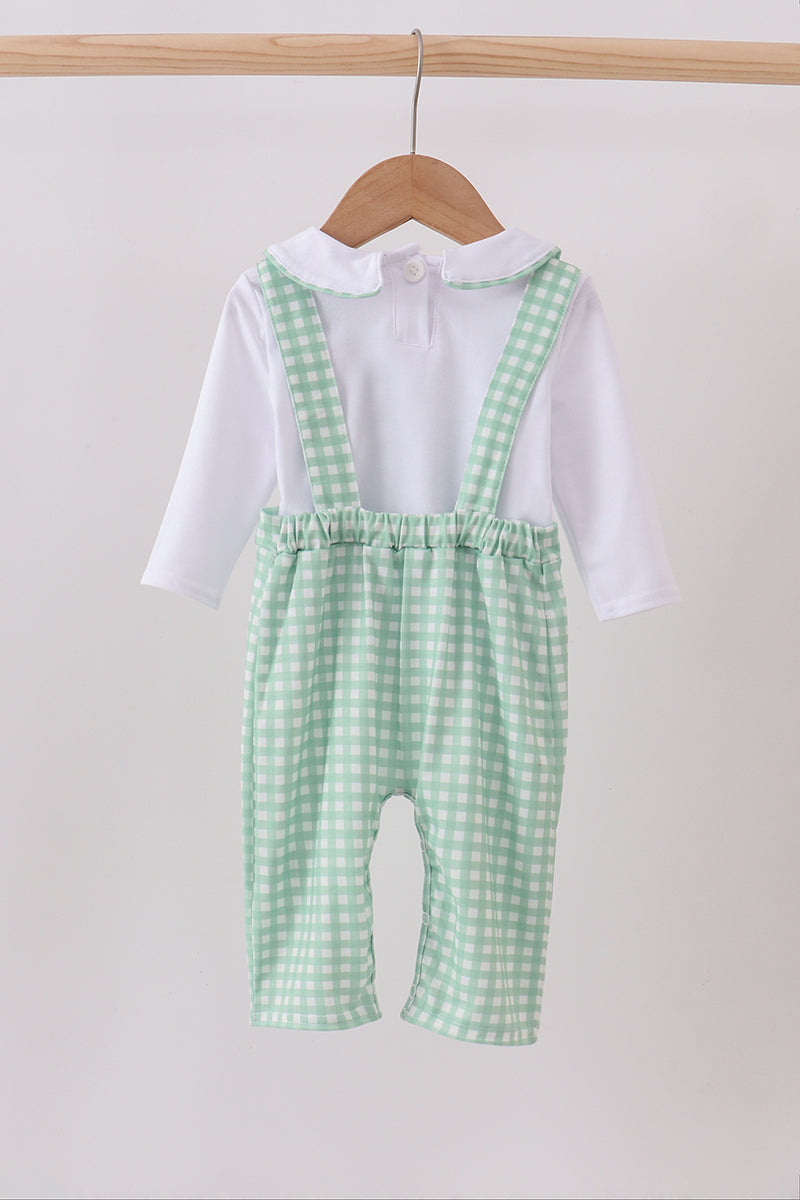 Green checkered romper with white shirt on a wooden hanger against a light gray background