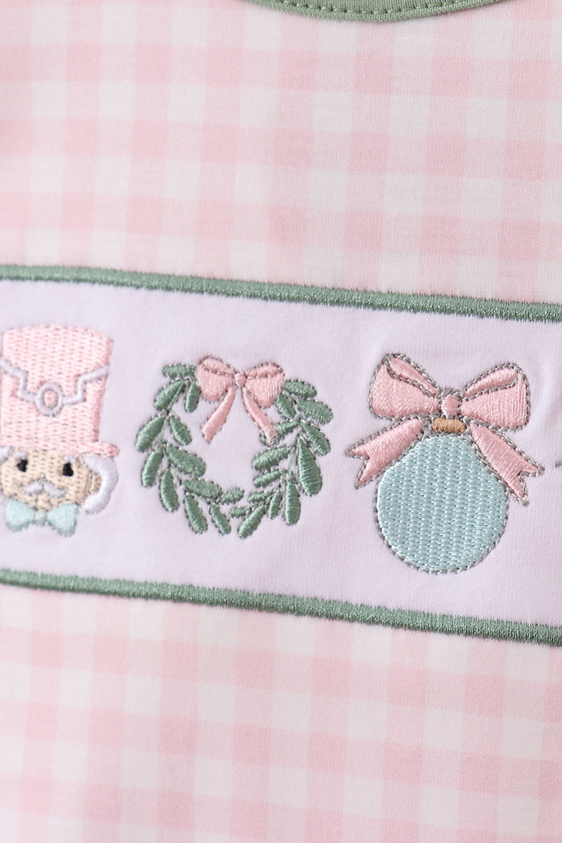 Embroidered design on a pink fabric with a character, wreath, and ornament.