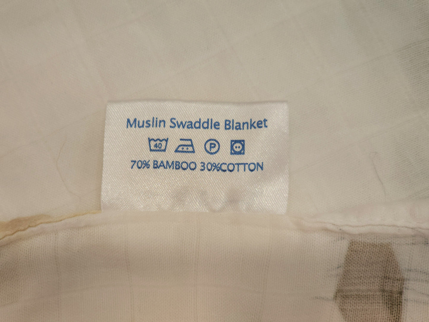 Label on a muslin swaddle blanket indicating material composition and care instructions.