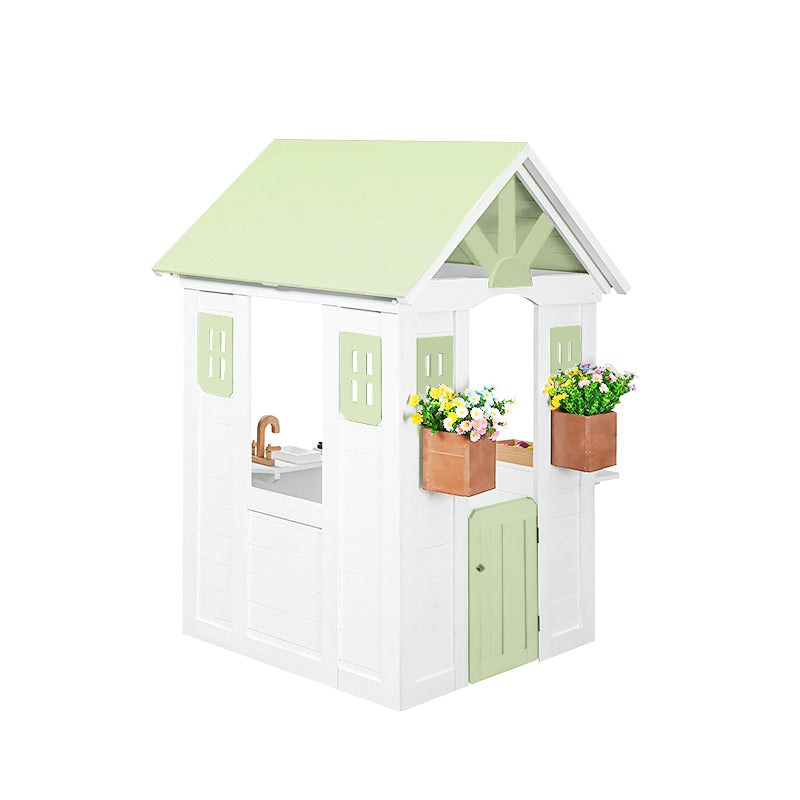 Children's playhouse with a green roof and white body, featuring flower pots and a sink.