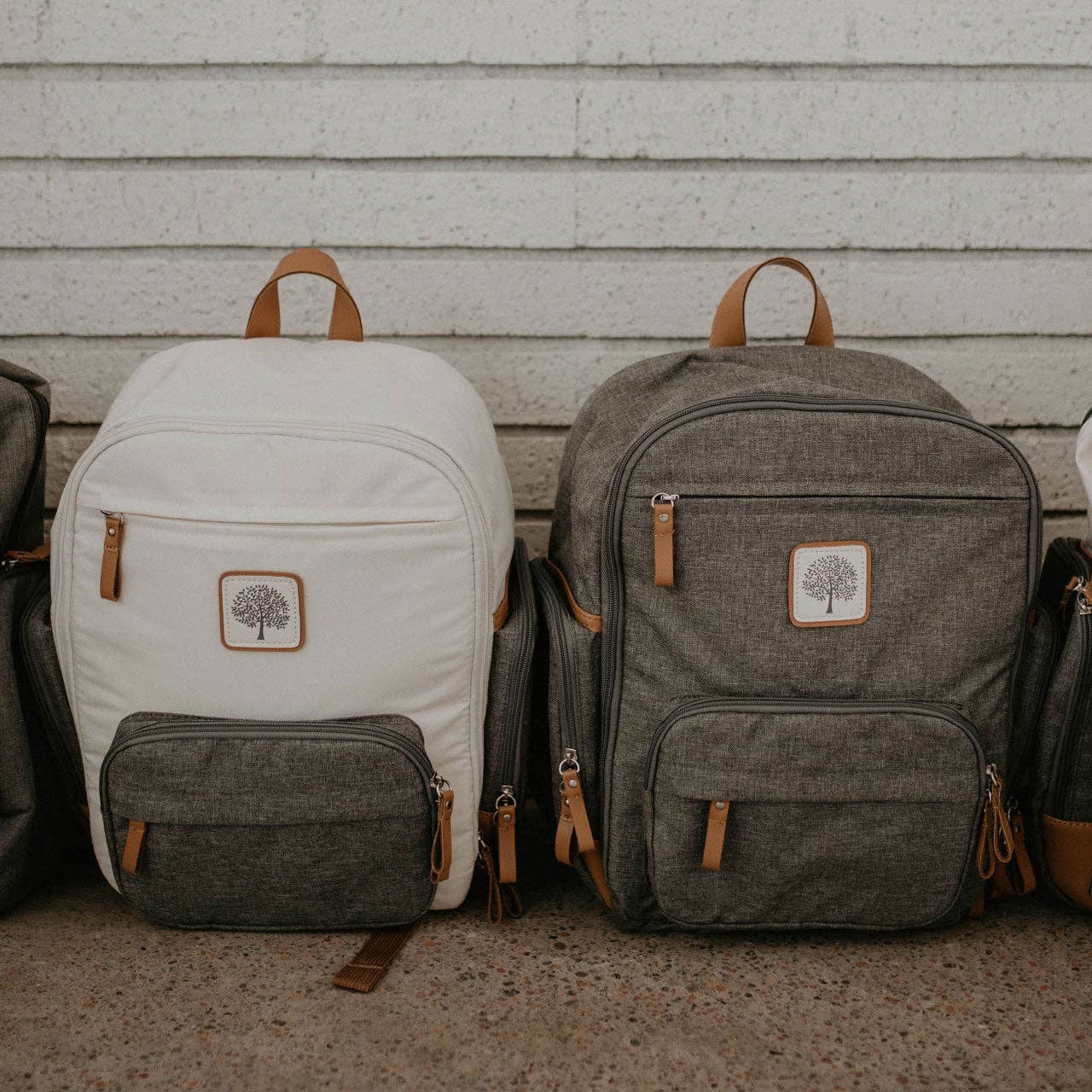 Two backpacks, one white and one gray, with a tree logo on a neutral background.