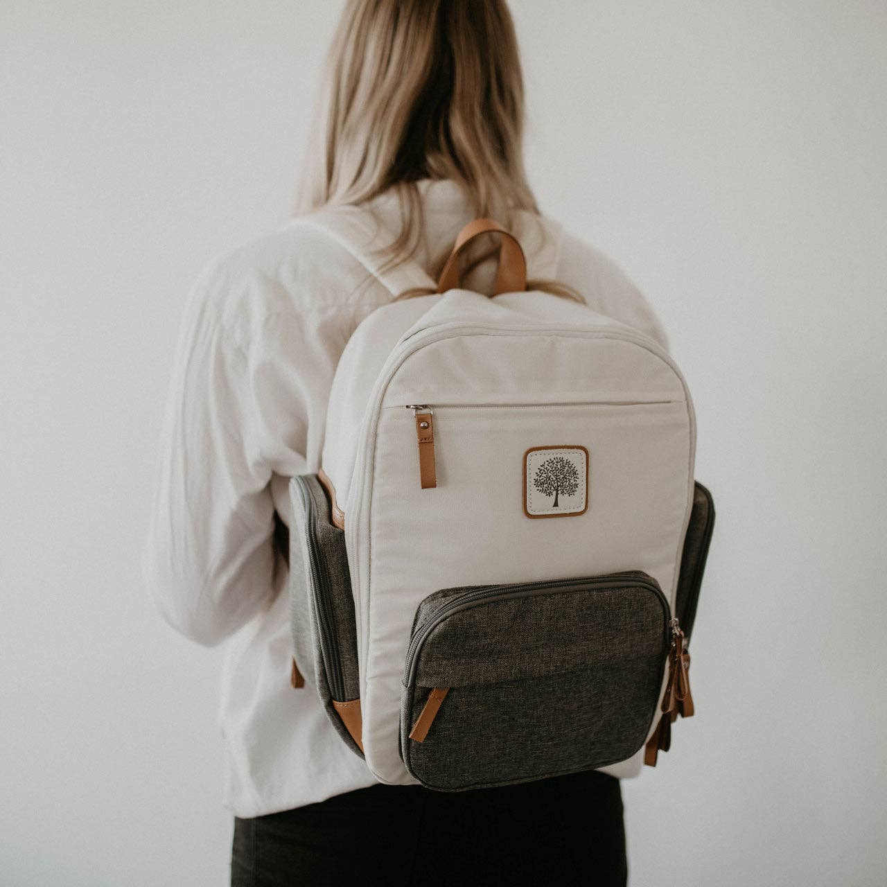 Person wearing a beige backpack with a tree logo.