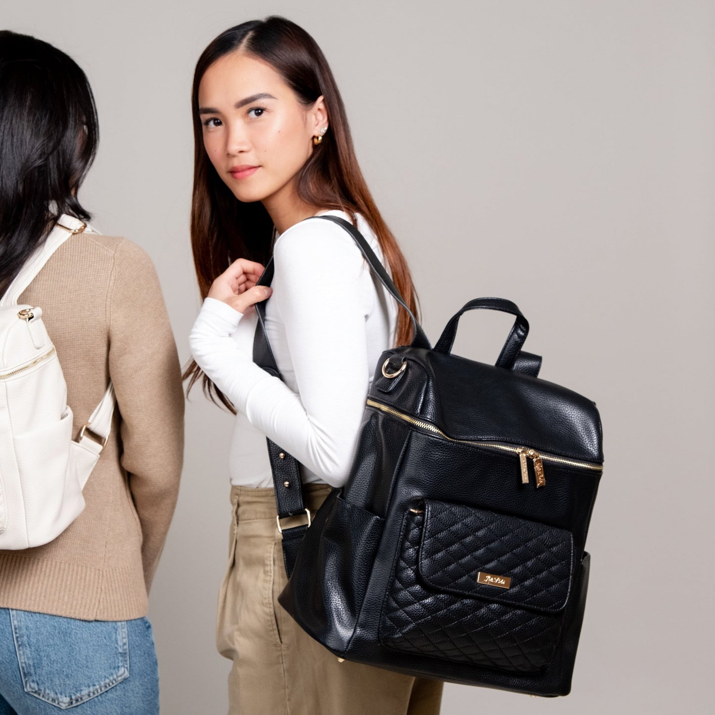 Two women with backpacks, one holding a black quilted backpack.