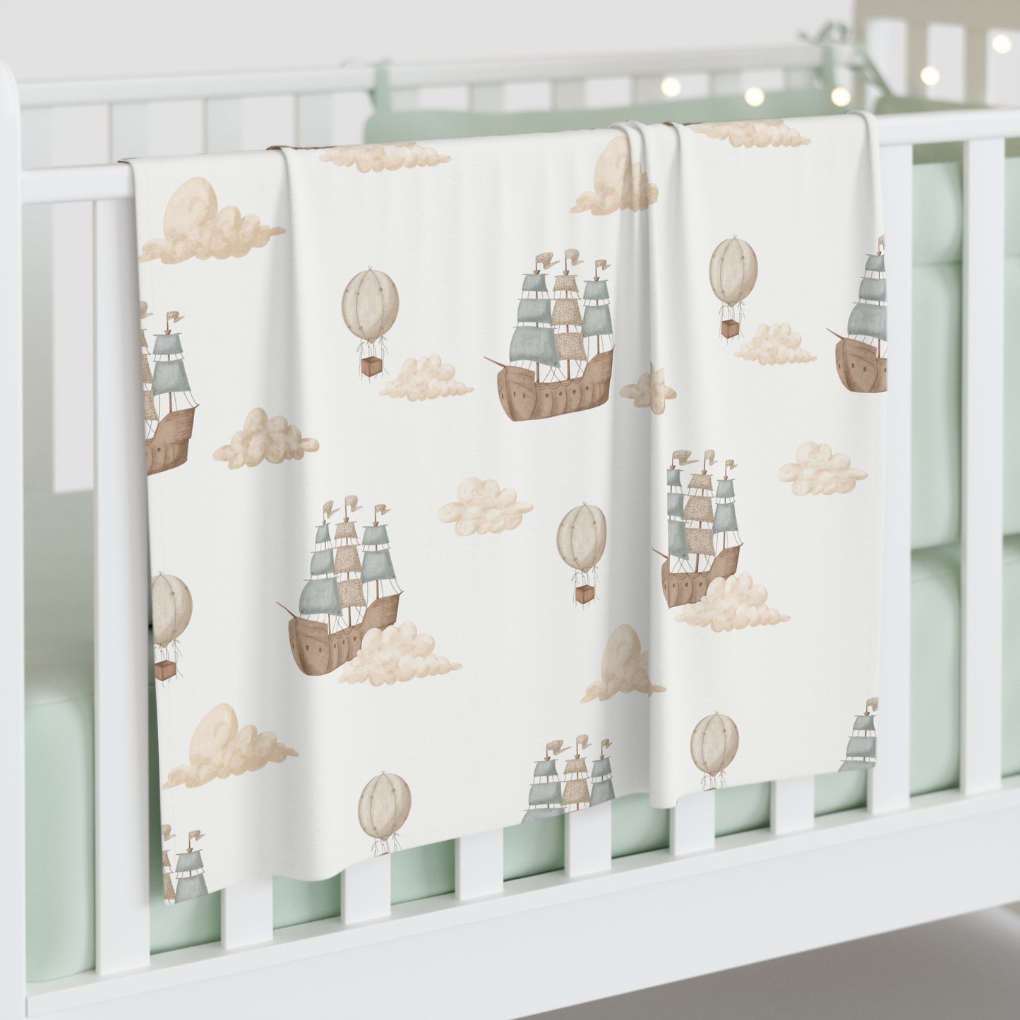 Baby crib with a decorative blanket featuring ship and hot air balloon patterns on a white background.
