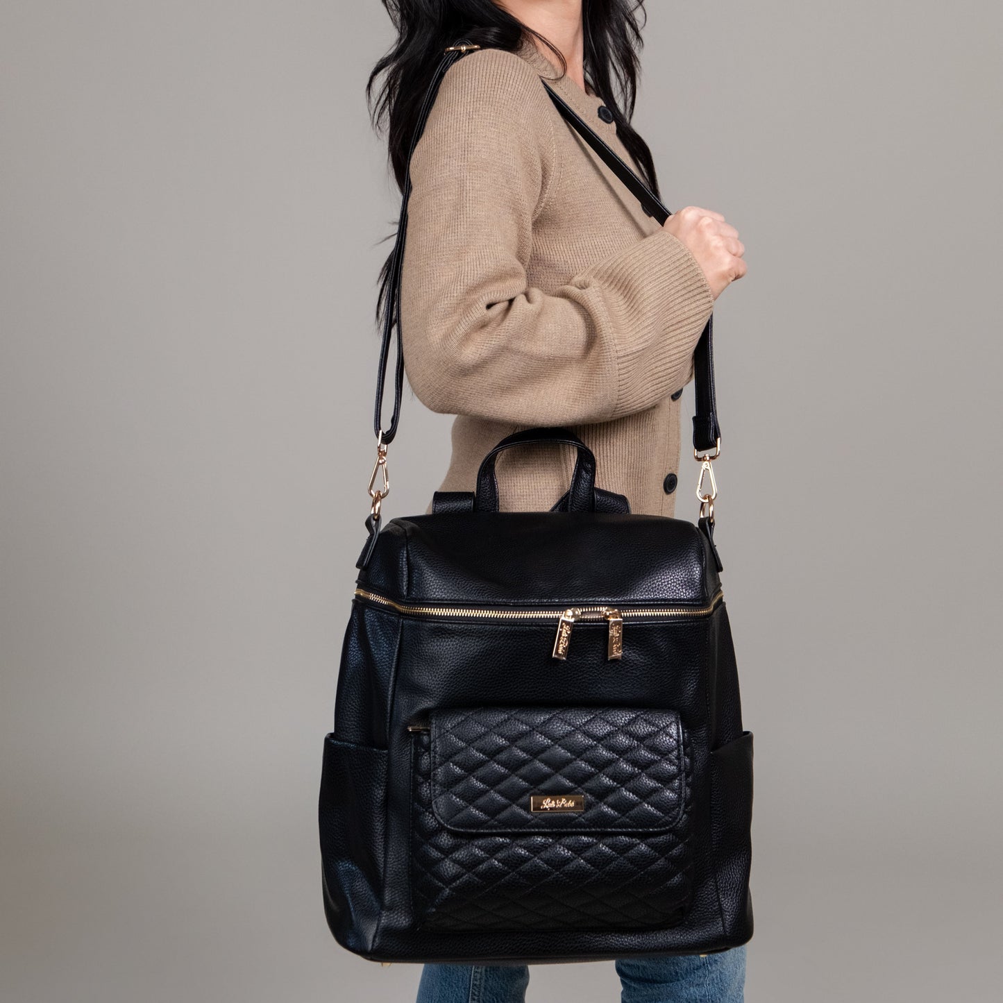 Black quilted backpack held by a person against a gray background