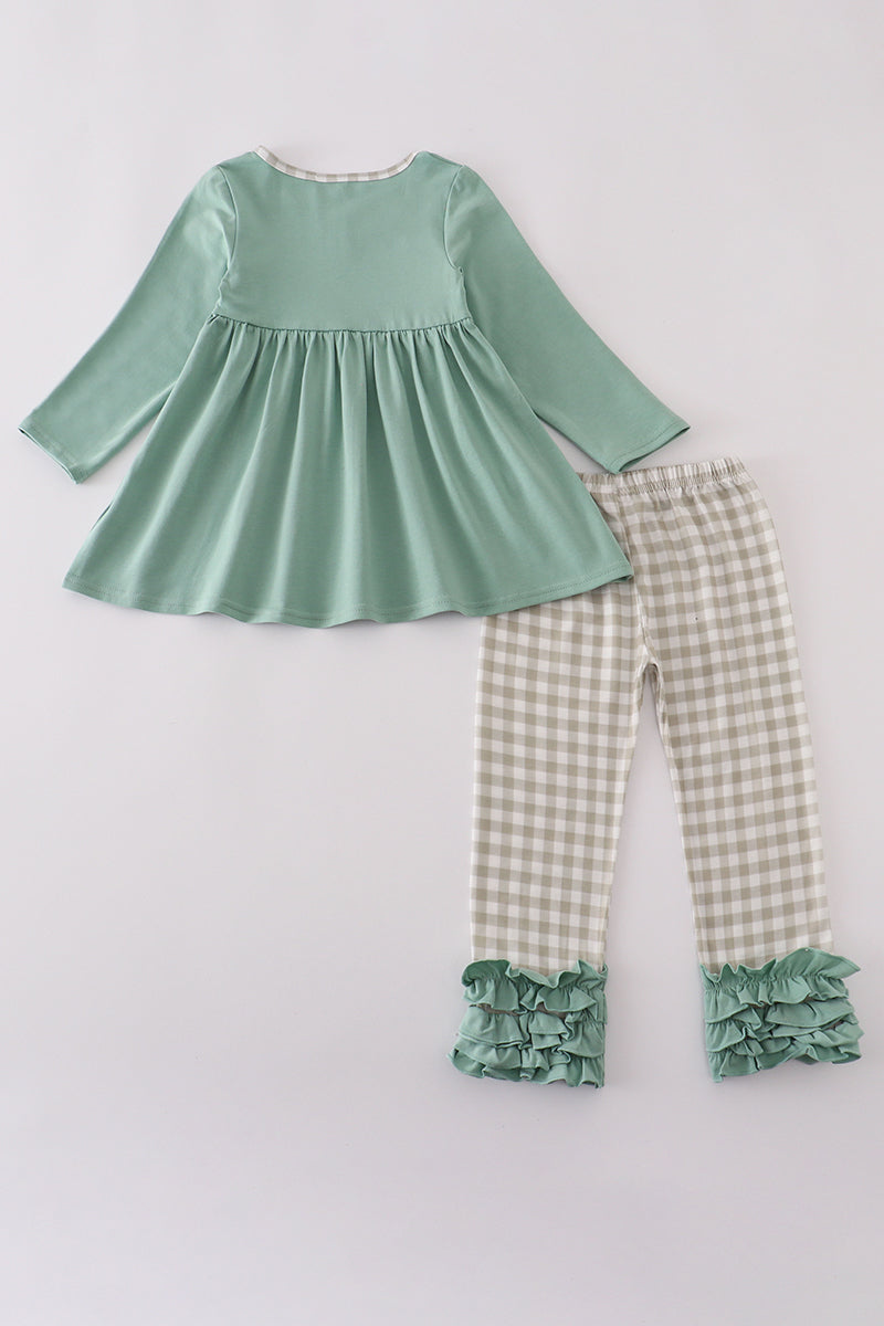 Green top and checkered pants with ruffles on a light gray background