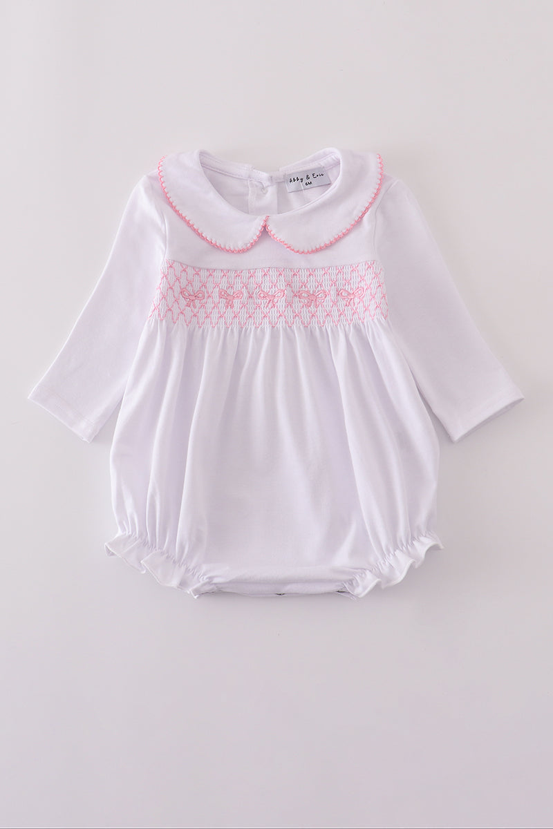White baby romper with pink smocking on a light gray background