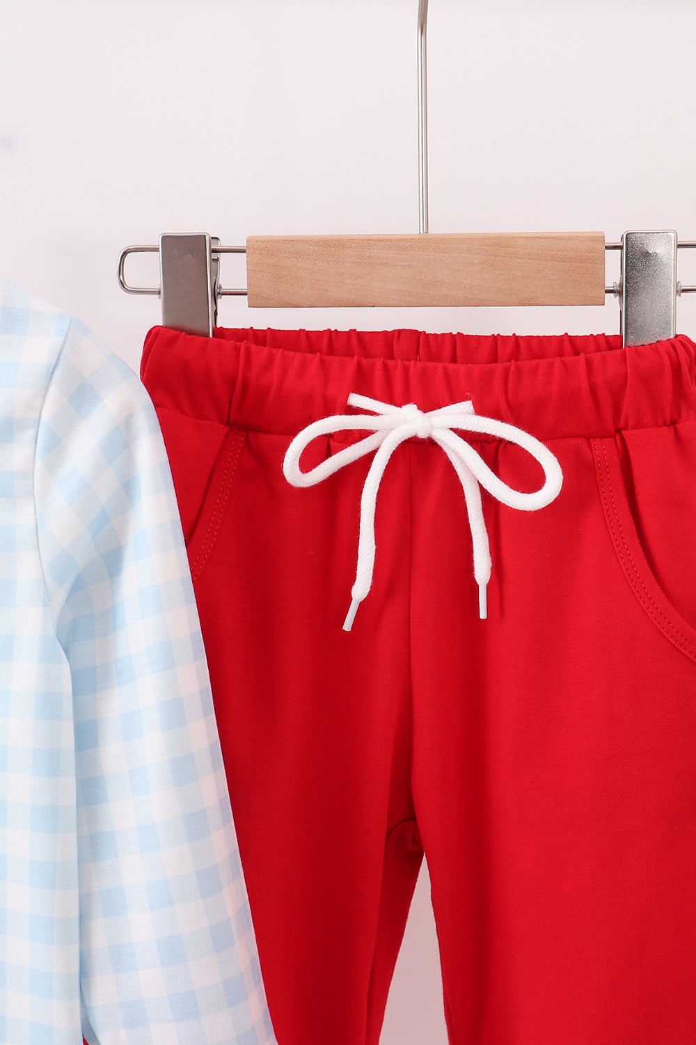 Red pants with a white drawstring on a hanger against a light background