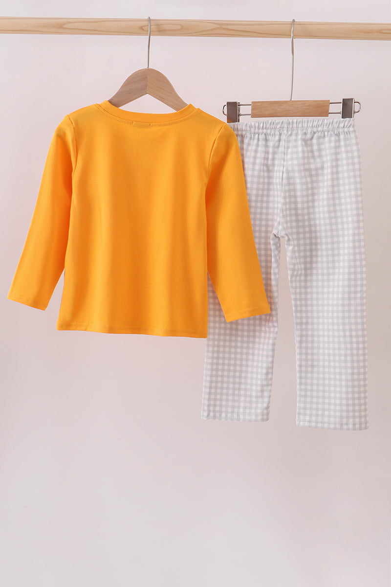 Yellow long-sleeve shirt and checkered pants hanging on a wooden rod against a light pink background.
