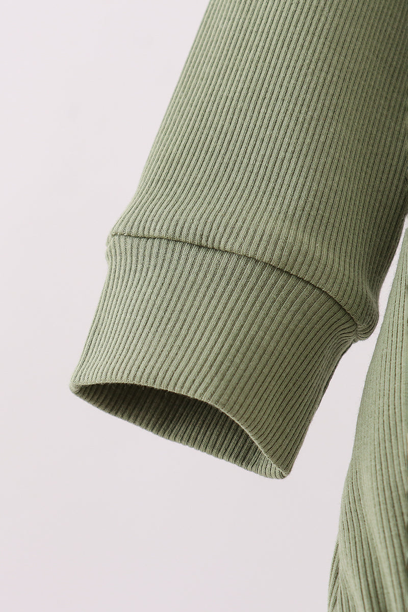 Close-up of a green ribbed sweater sleeve on a light gray background