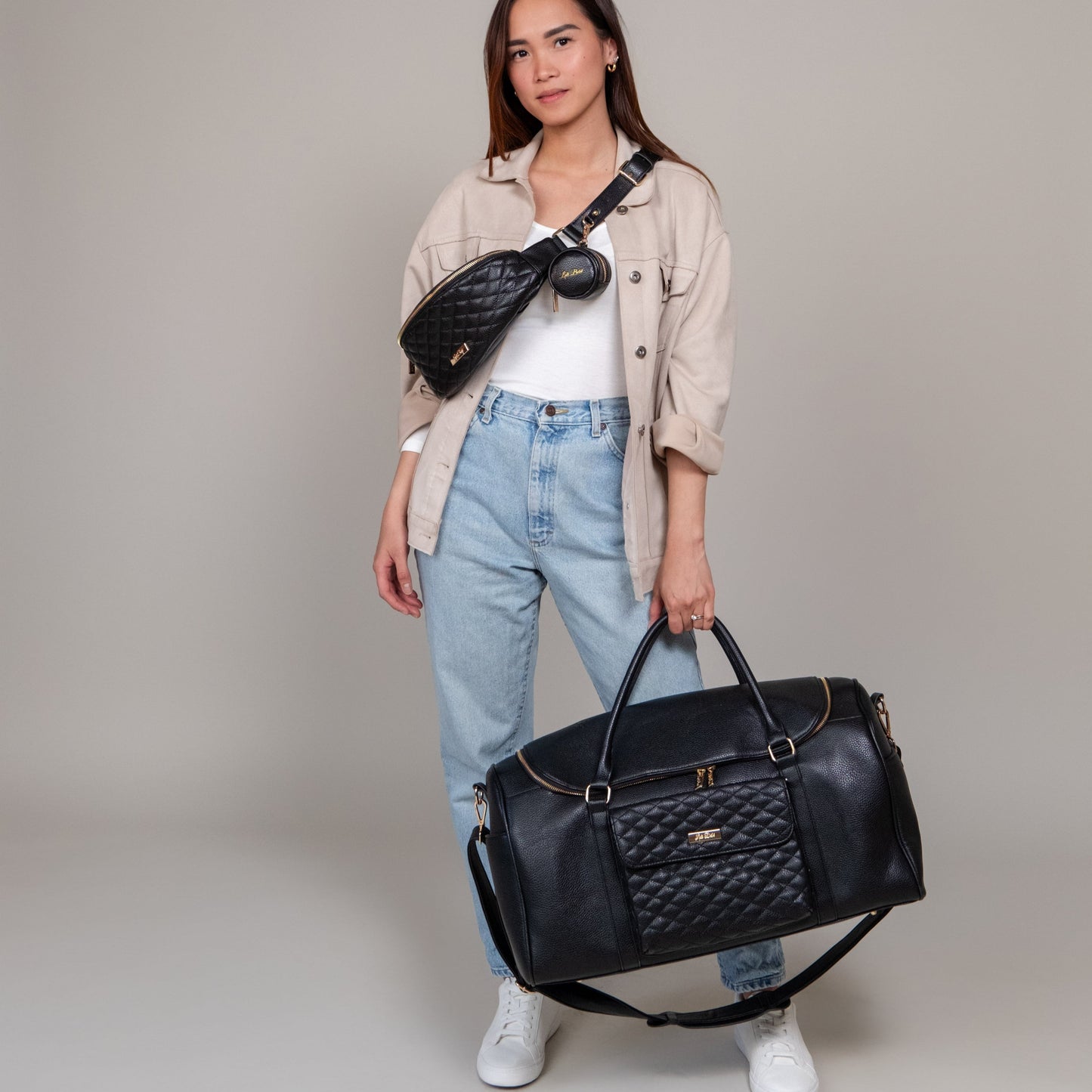 Woman holding a black quilted handbag against a plain background
