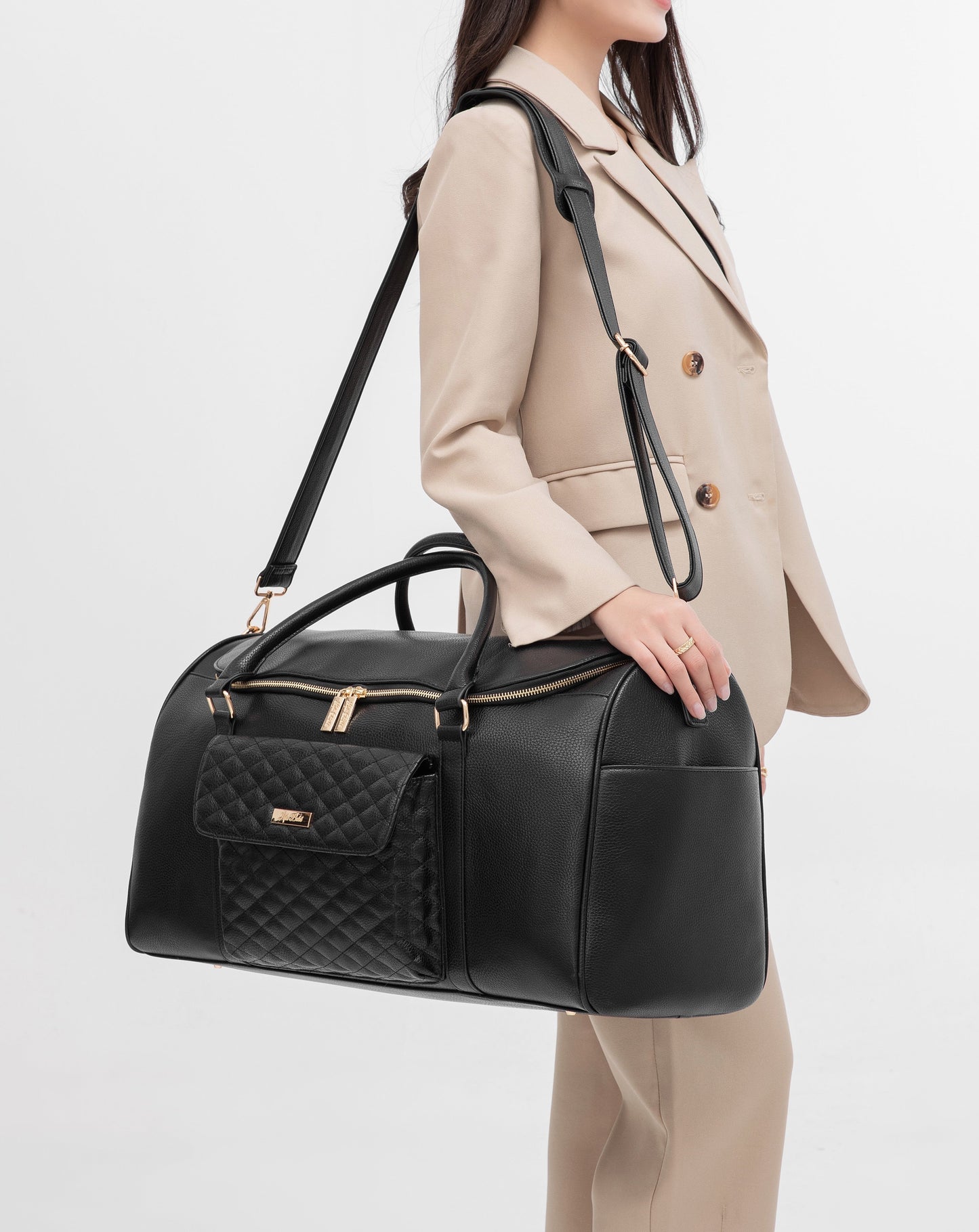 Person holding a black quilted handbag with a beige coat on a light gray background