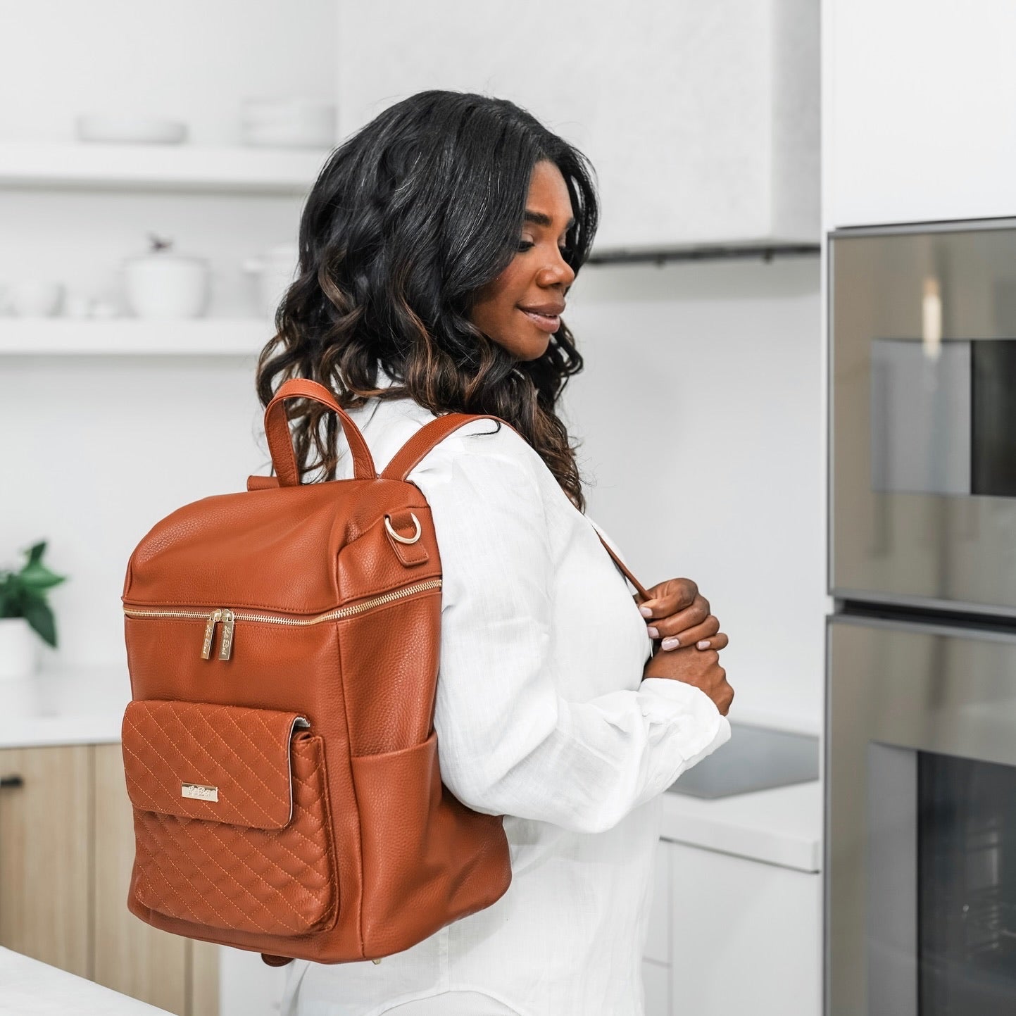Woman wearing a brown leather backpack in a kitchen setting