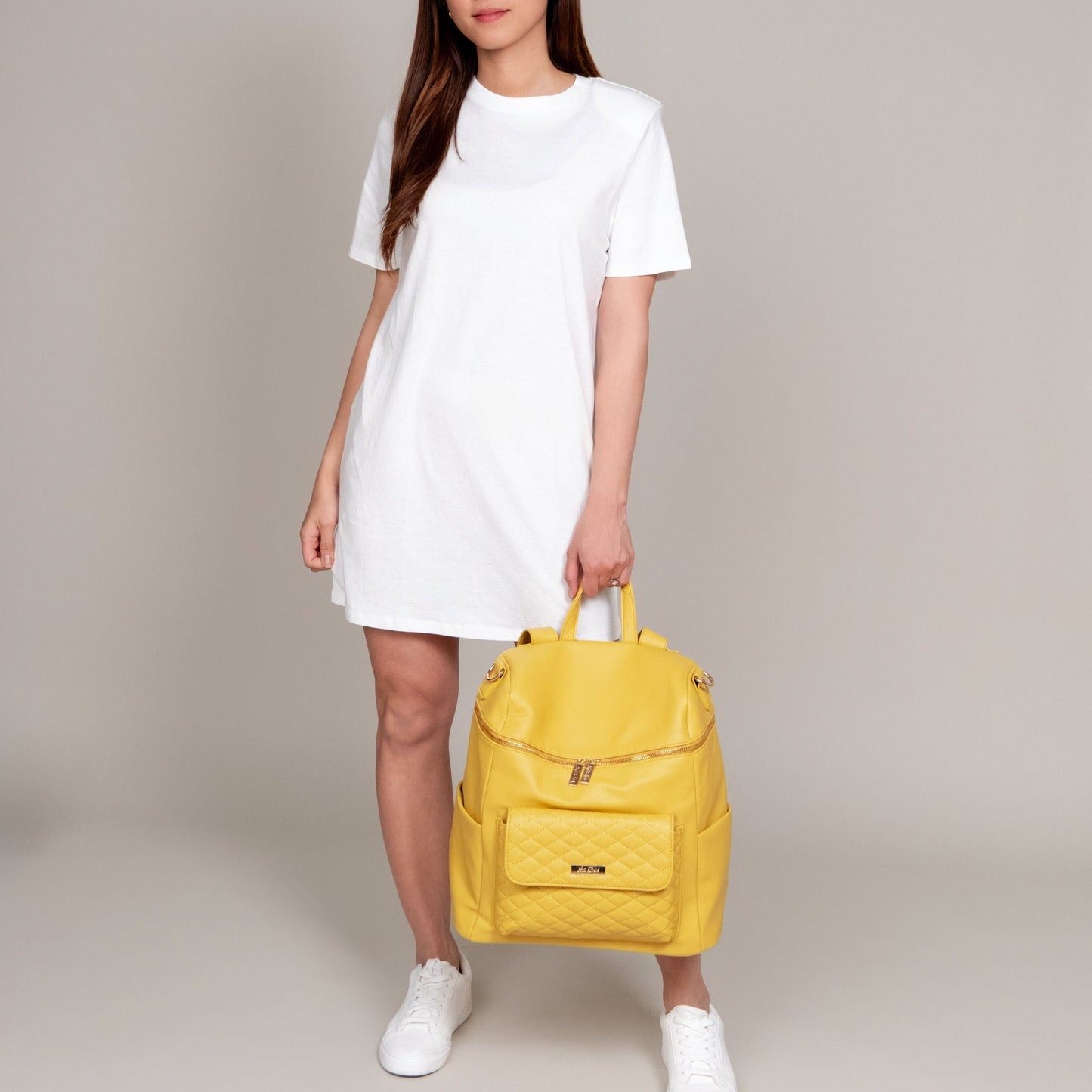 Person holding a yellow backpack against a neutral background