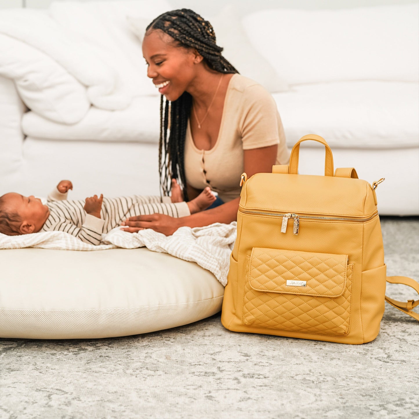 Woman sitting on the floor with a baby and a yellow backpack next to them