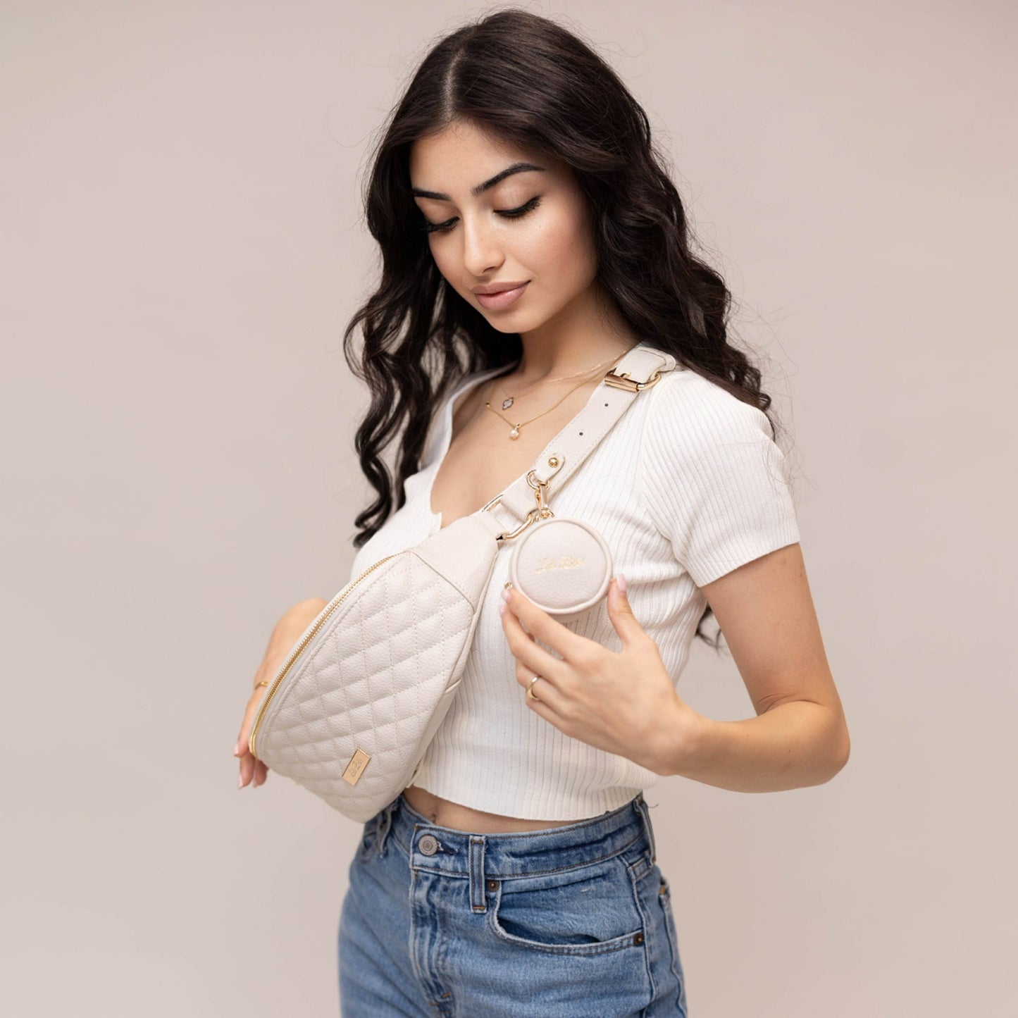 Woman holding a white quilted handbag against a plain background