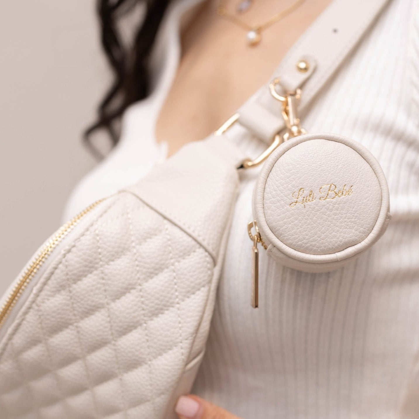 Round beige pouch with 'Little Belle' branding attached to a white jacket.