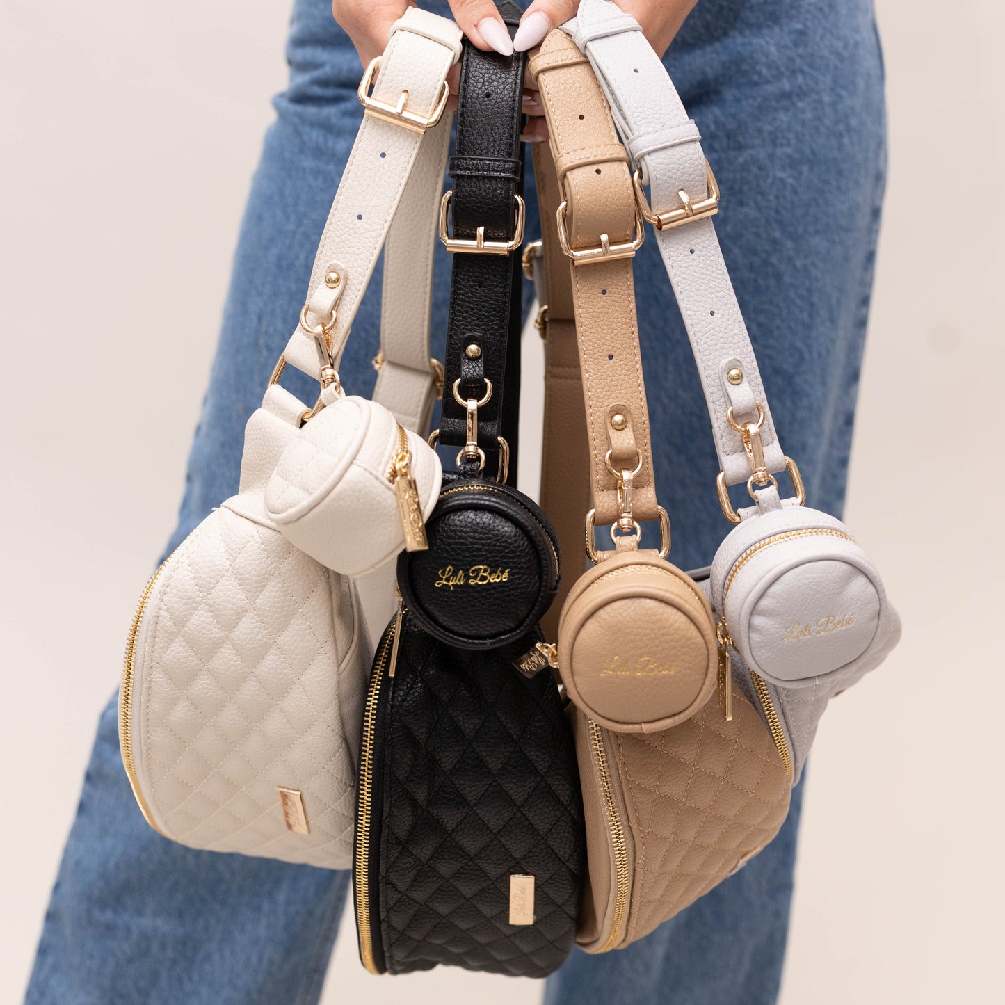 Four small handbags with different colors and designs held by a person wearing blue jeans.