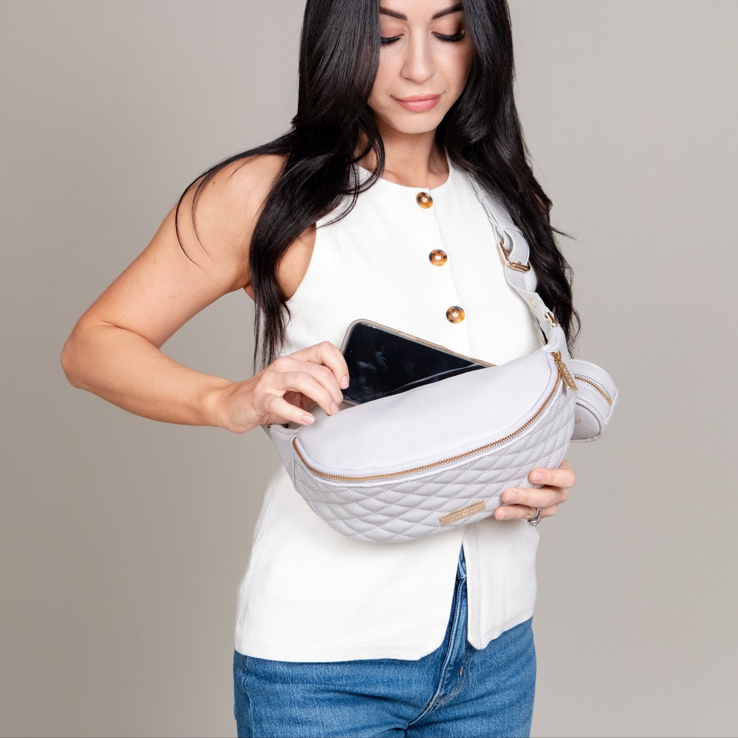 Woman holding a white quilted waist bag with a gray background