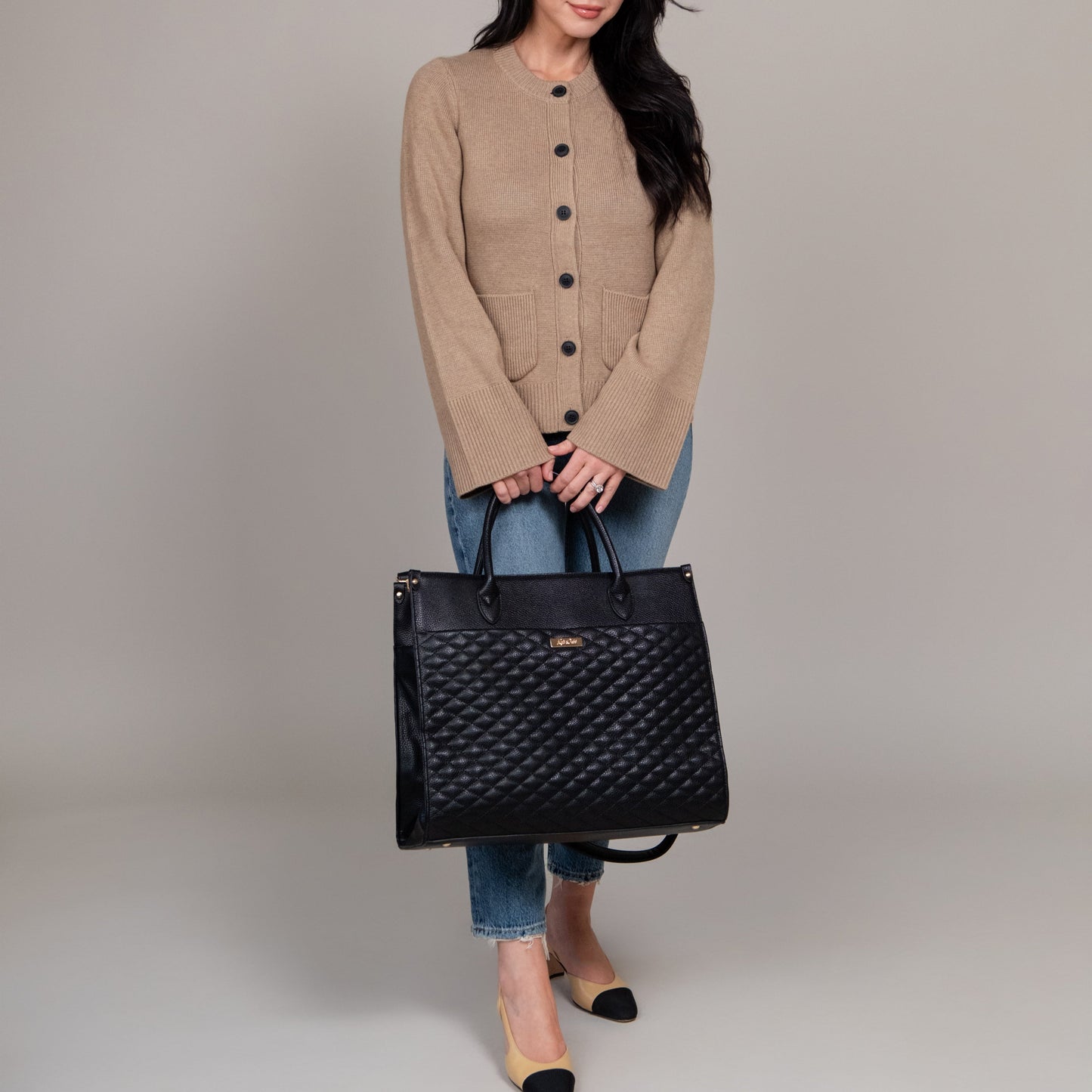 Woman holding a black quilted handbag against a plain background