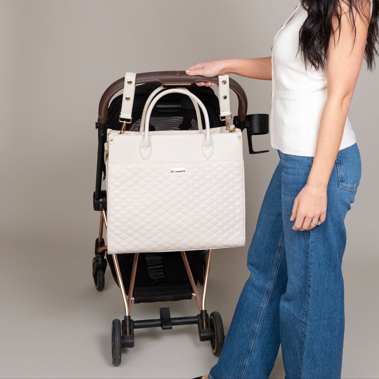 Woman pushing a stroller with a white quilted handbag attached to it.