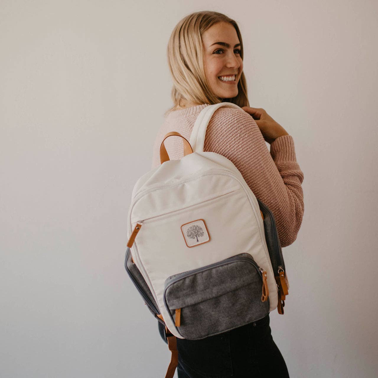 Person wearing a white backpack with a logo, smiling.