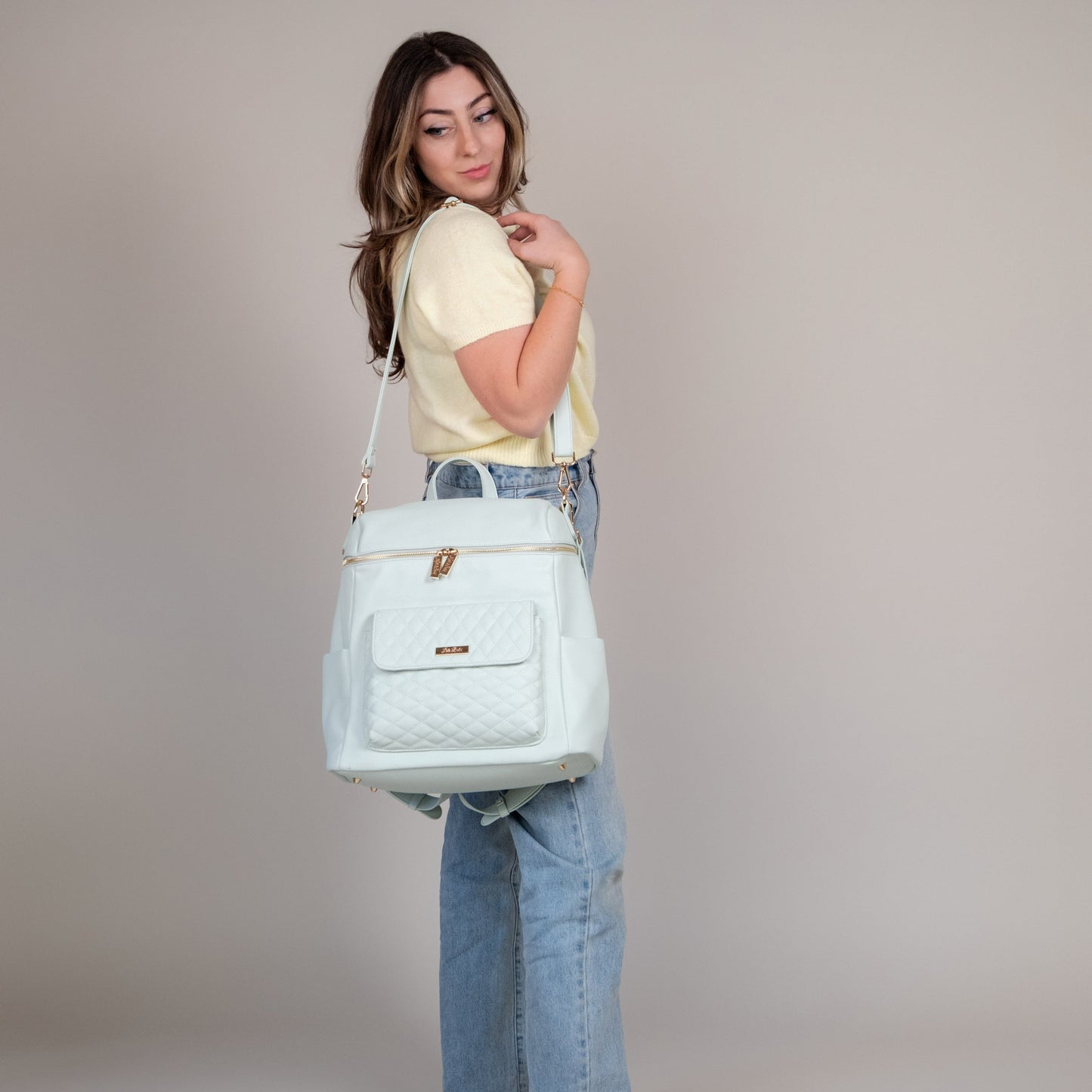Woman holding a light blue quilted handbag against a plain background