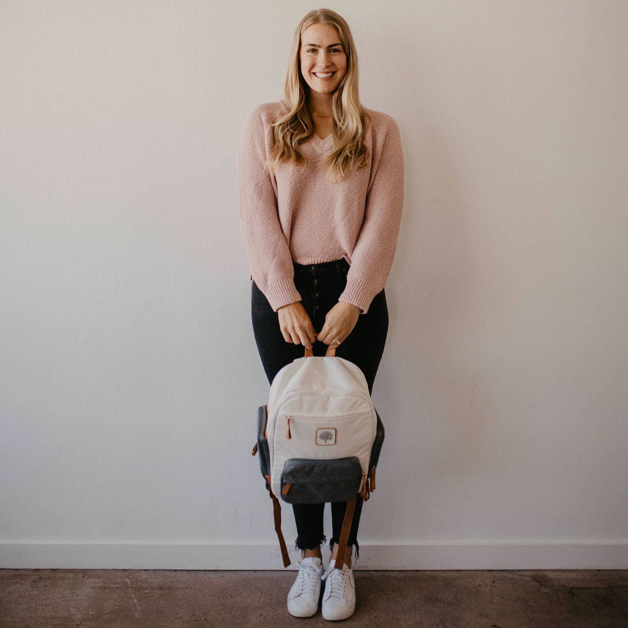 Woman holding a white backpack against a plain background