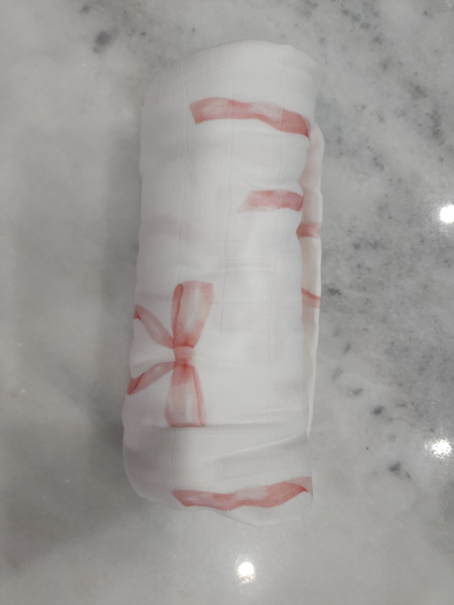 Rolled Swaddle blanket with pink bow designs on a marble surface