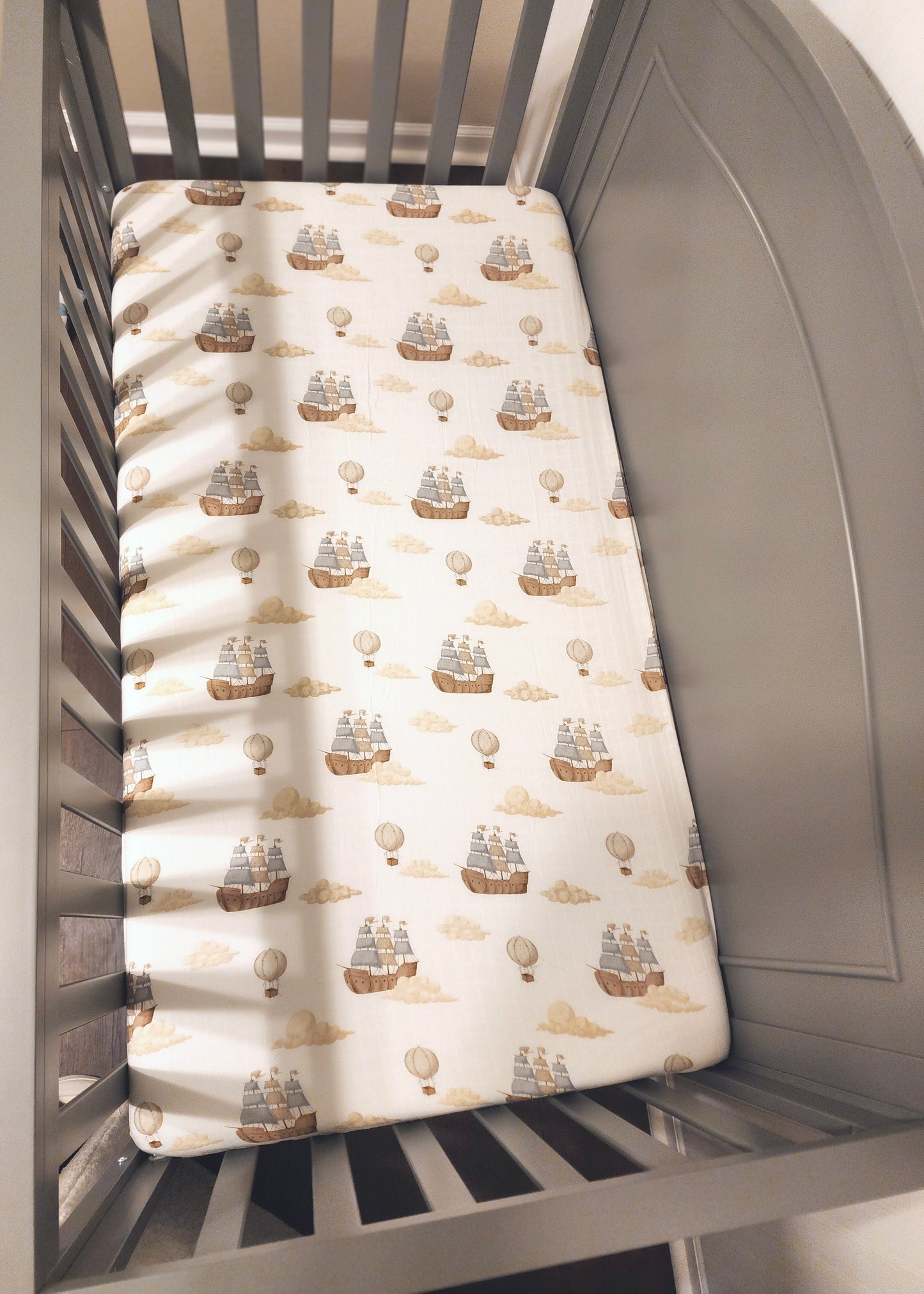 Crib with a fitted sheet featuring ship and hot air balloon pattern