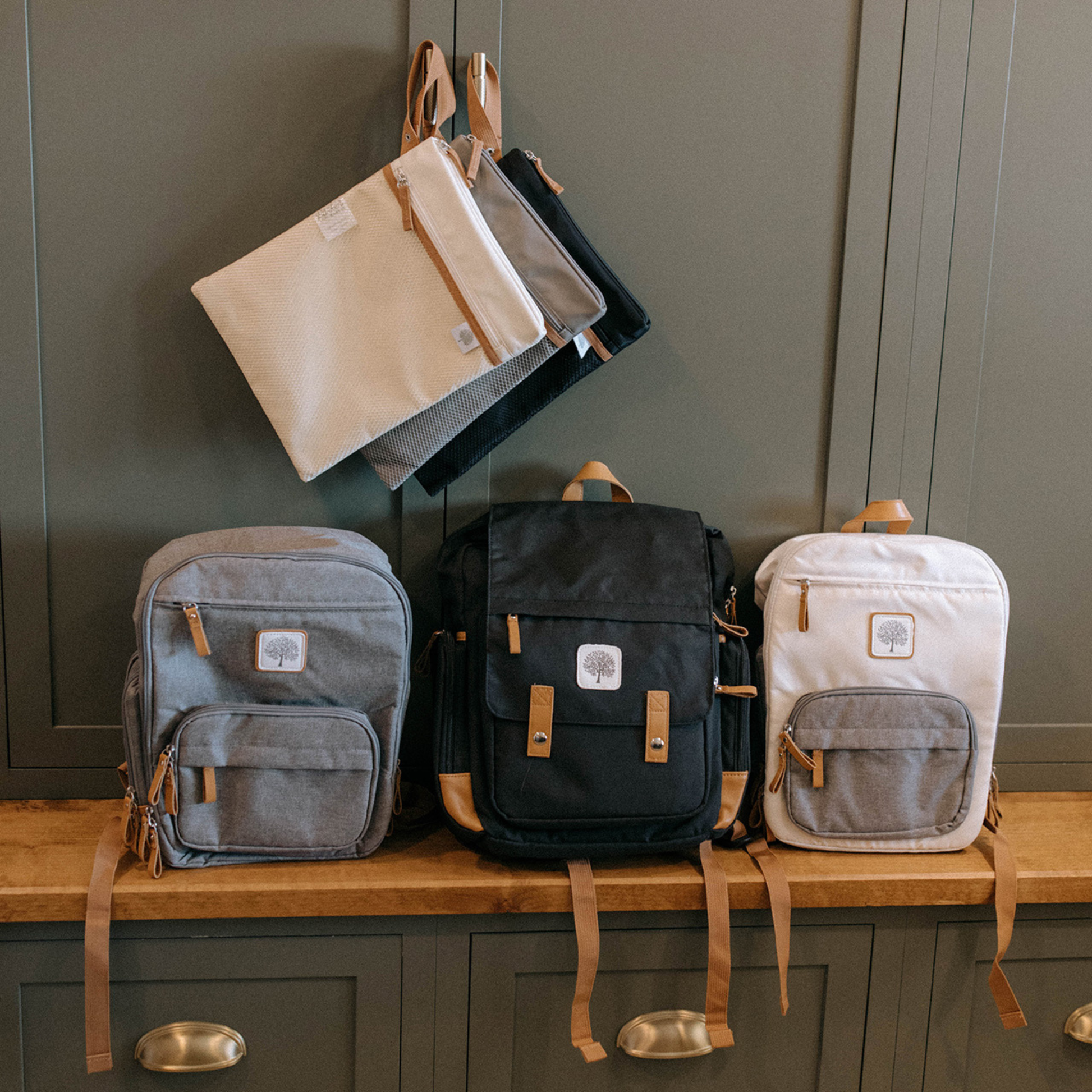 Collection of backpacks and a laptop bag on a wooden surface against a dark green cabinet.