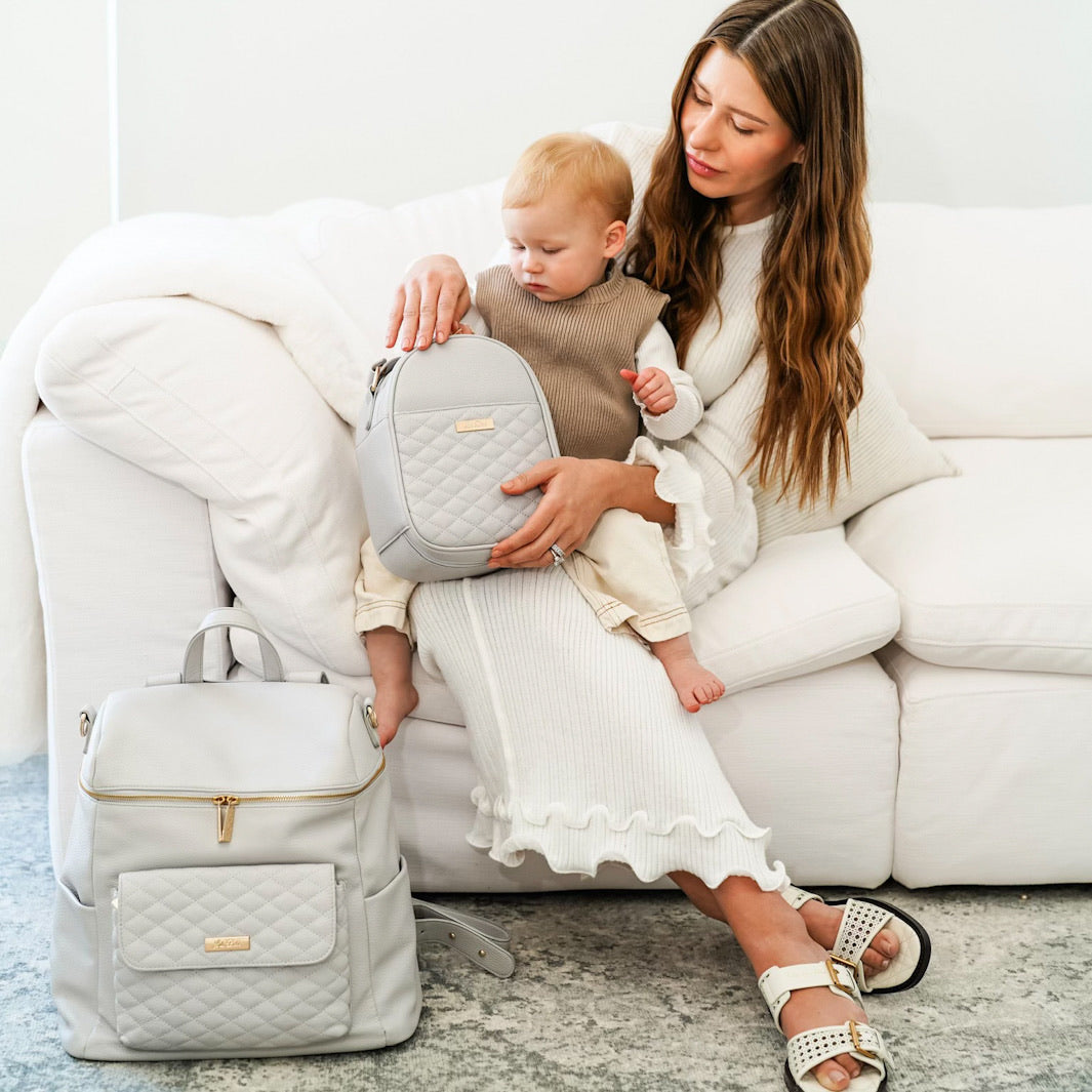 Woman holding a baby and a gray backpack on a white couch