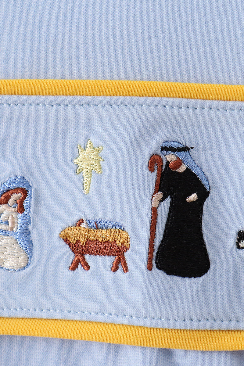 Embroidered nativity scene on a light blue fabric with yellow trim.