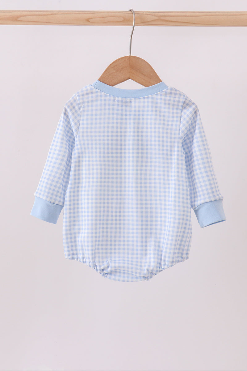 Blue checkered baby romper on a wooden hanger against a beige wall.