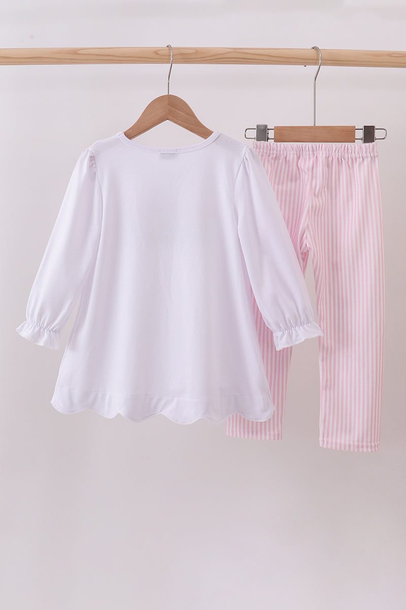 White blouse and pink striped pants hanging on a wooden rack against a white background