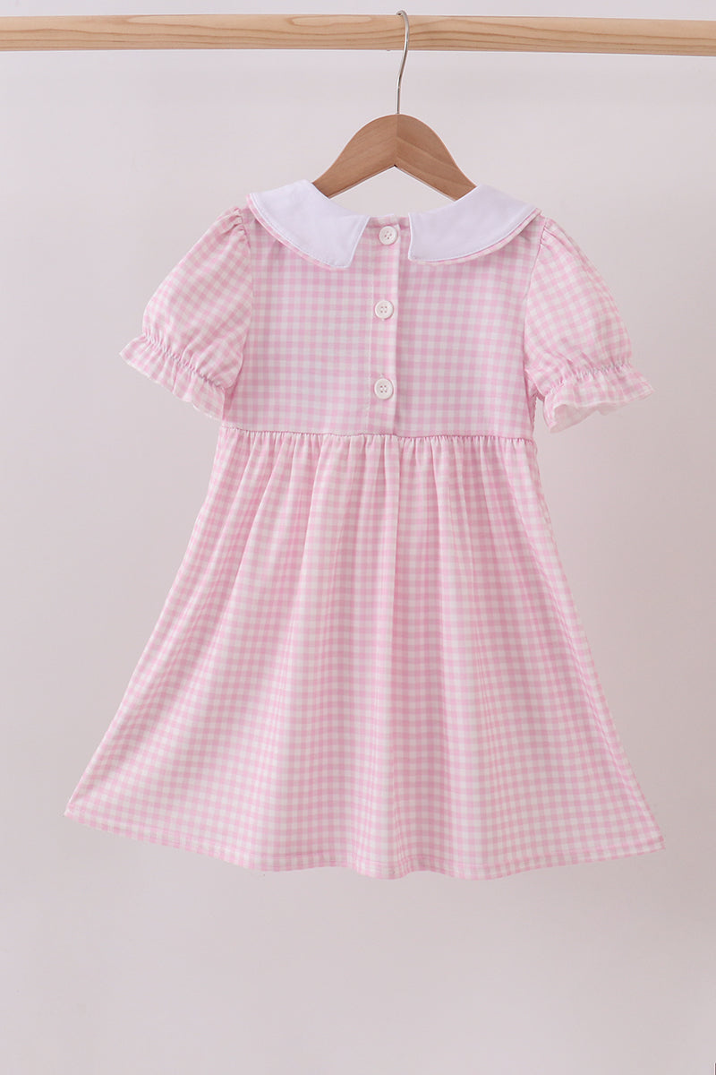 Pink checkered dress with white collar on a wooden hanger against a light gray background