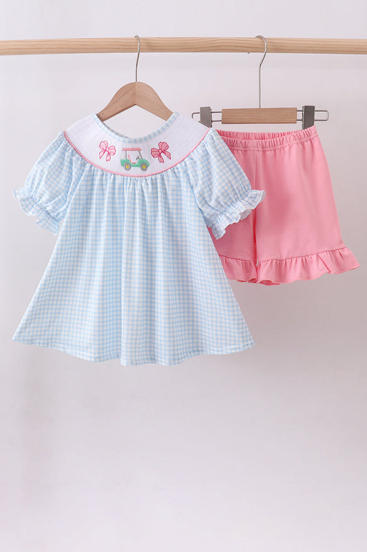Children's light blue checkered dress with embroidered collar and pink shorts on a wooden hanger against a white background.