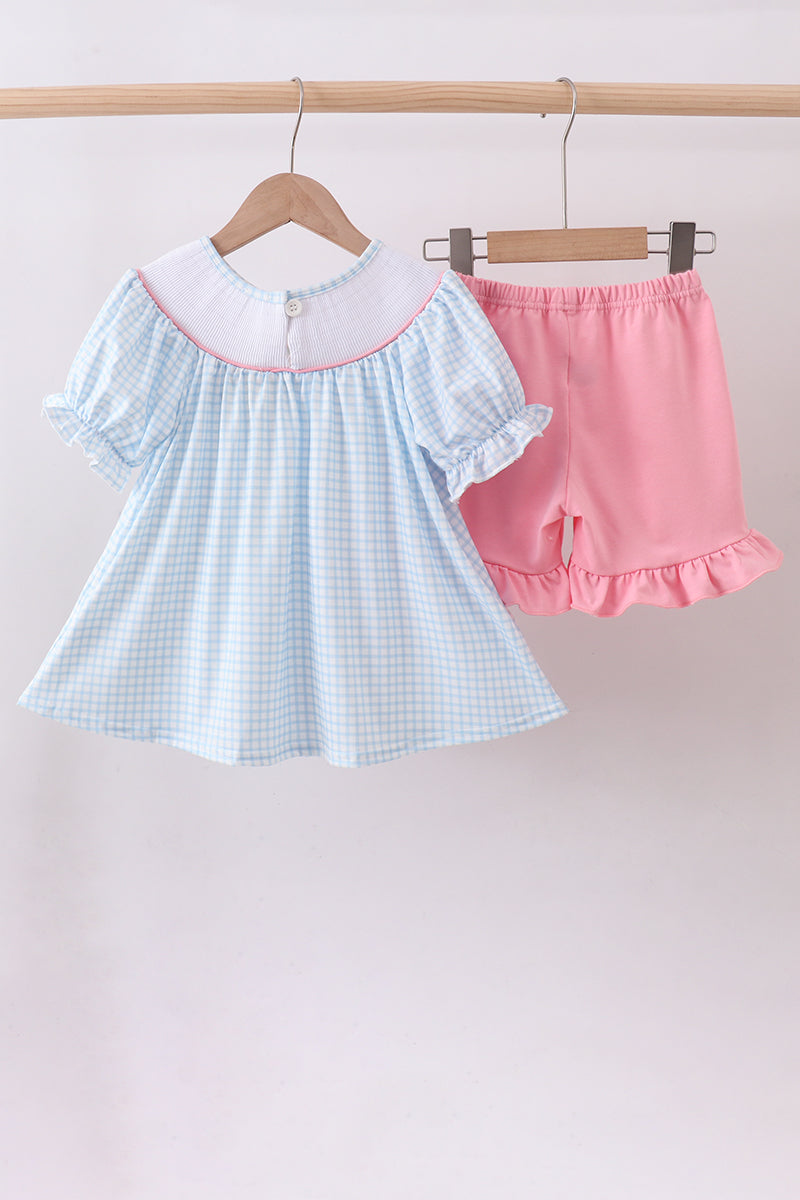 Light blue checkered dress with white collar and pink shorts on hangers against a light background