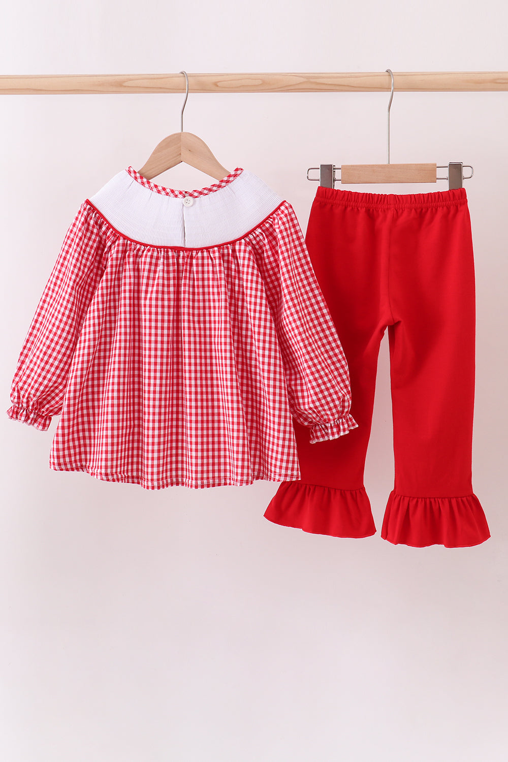 Red checkered dress with white collar and red pants on hangers against a white background