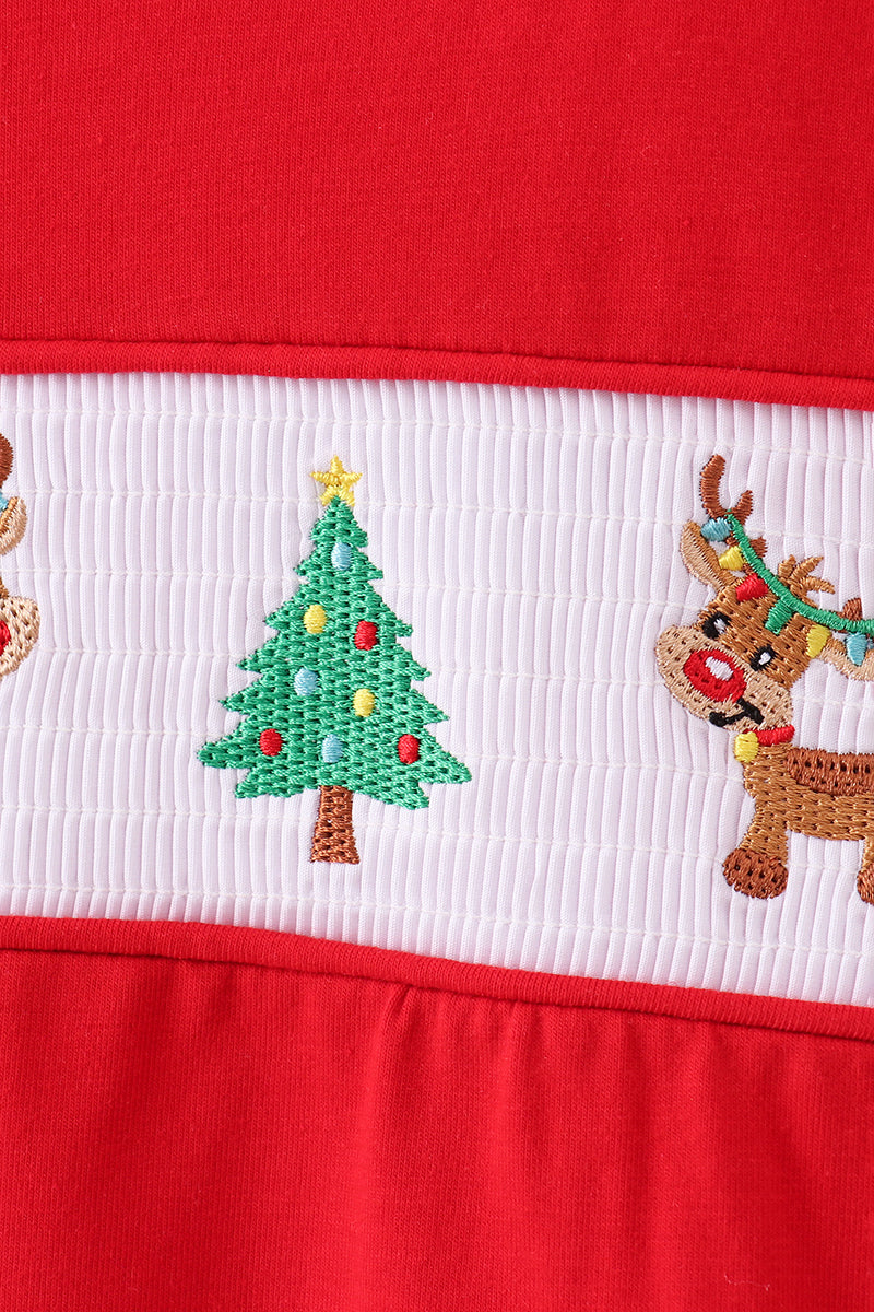 Close-up of a red fabric with embroidered Christmas tree and reindeer design.