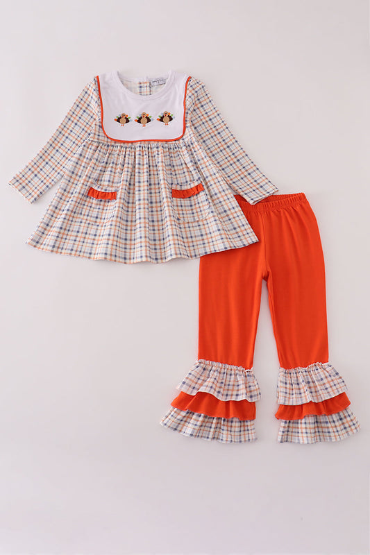 Children's outfit with plaid dress and orange pants on a light gray background