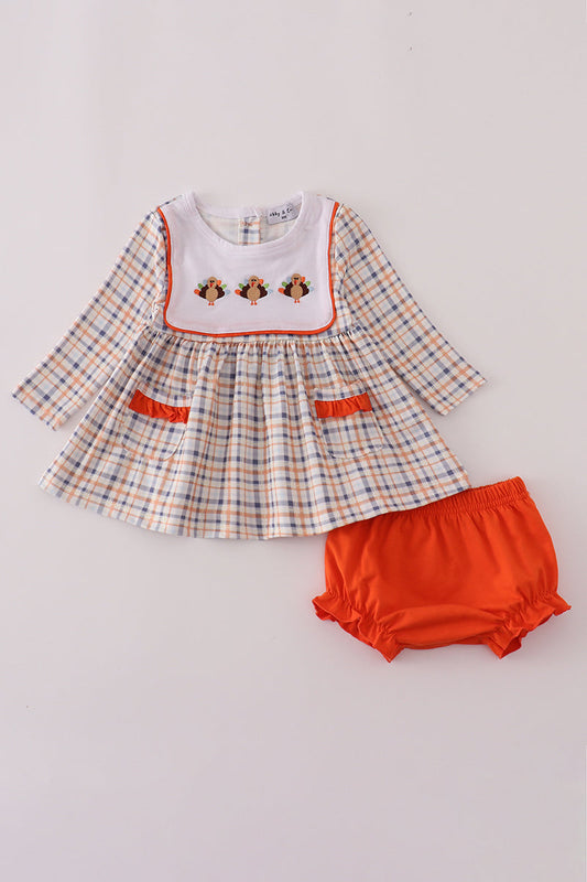 Baby dress with plaid pattern and orange bloomers on a light gray background