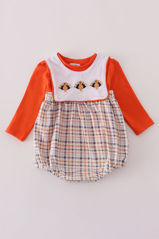Baby romper with orange long-sleeve top and plaid bottom on a light gray background