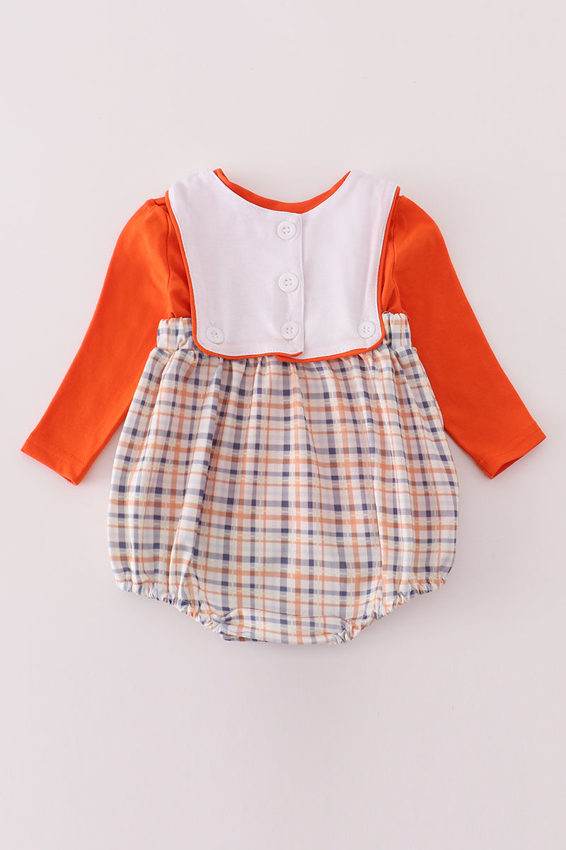 Baby romper with orange long-sleeve top and plaid skirt on a light gray background