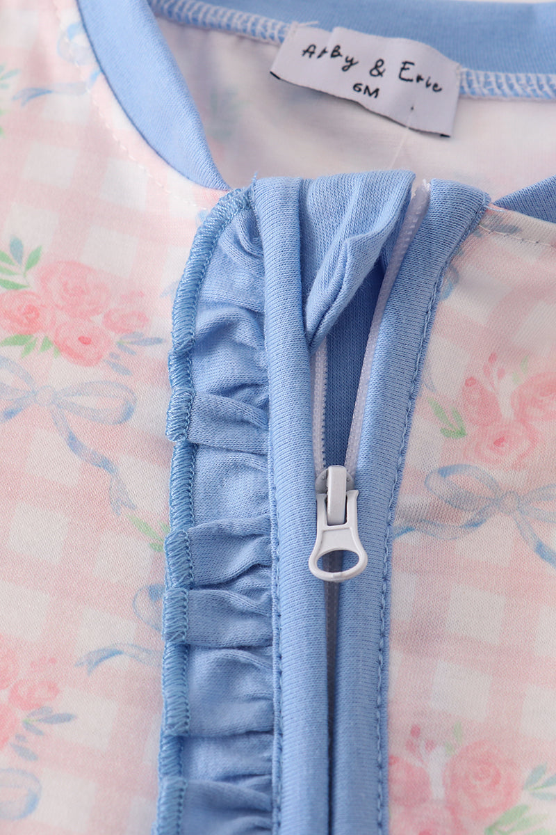 Close-up of a baby outfit with ruffled blue zipper and floral patterned background