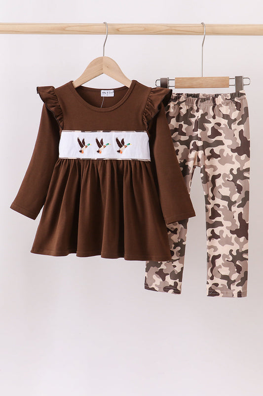 Brown dress with ruffled sleeves and white embroidery, paired with camouflage leggings, hanging on a wooden rack.
