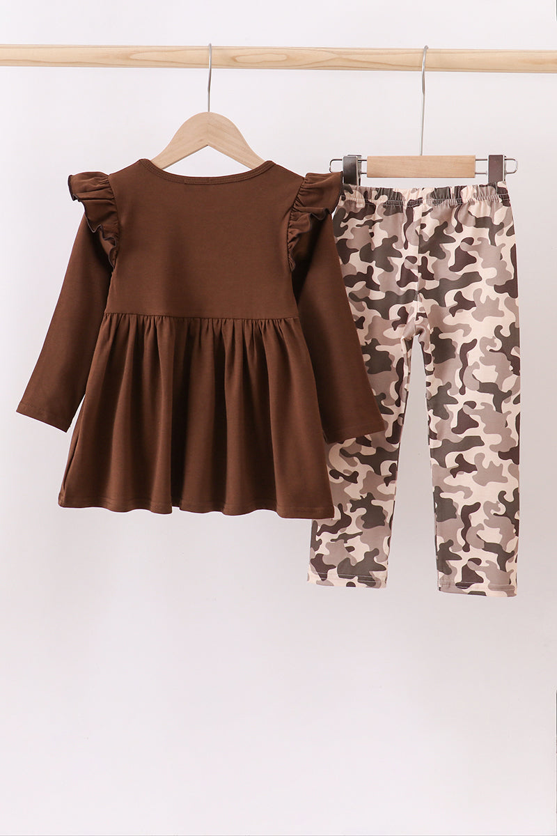 Brown dress with ruffled sleeves and camouflage pants on a hanger against a white background