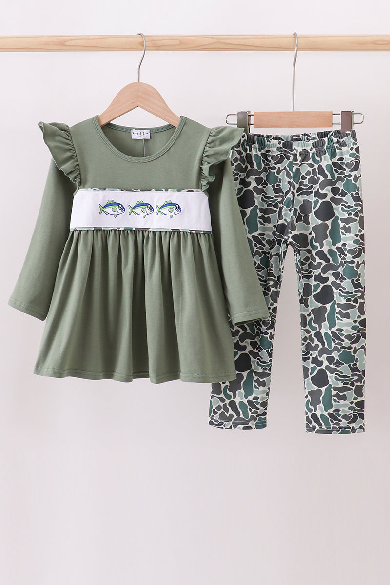 Green dress with ruffled sleeves and patterned leggings on a wooden rack against a white background