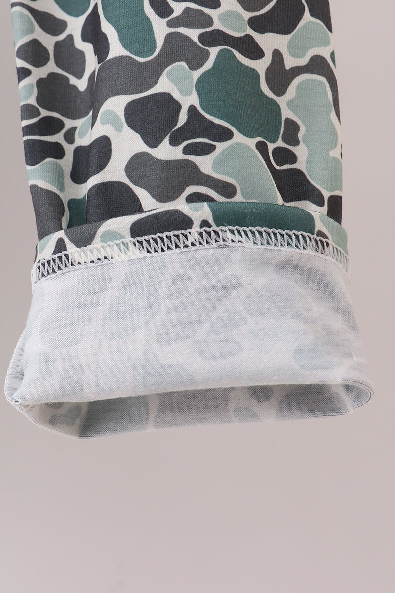 Close-up of a camouflage-patterned fabric with a white lace trim on a neutral background